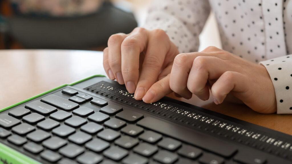 Eine blinde Frau benutzt einen Computer, der mit einer Braillezeile und einer Computertastatur ausgestattet ist.